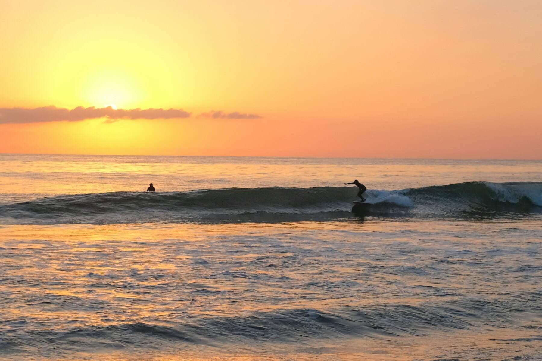 Un surfeur glisse sur une vague au coucher du soleil, vu de loin