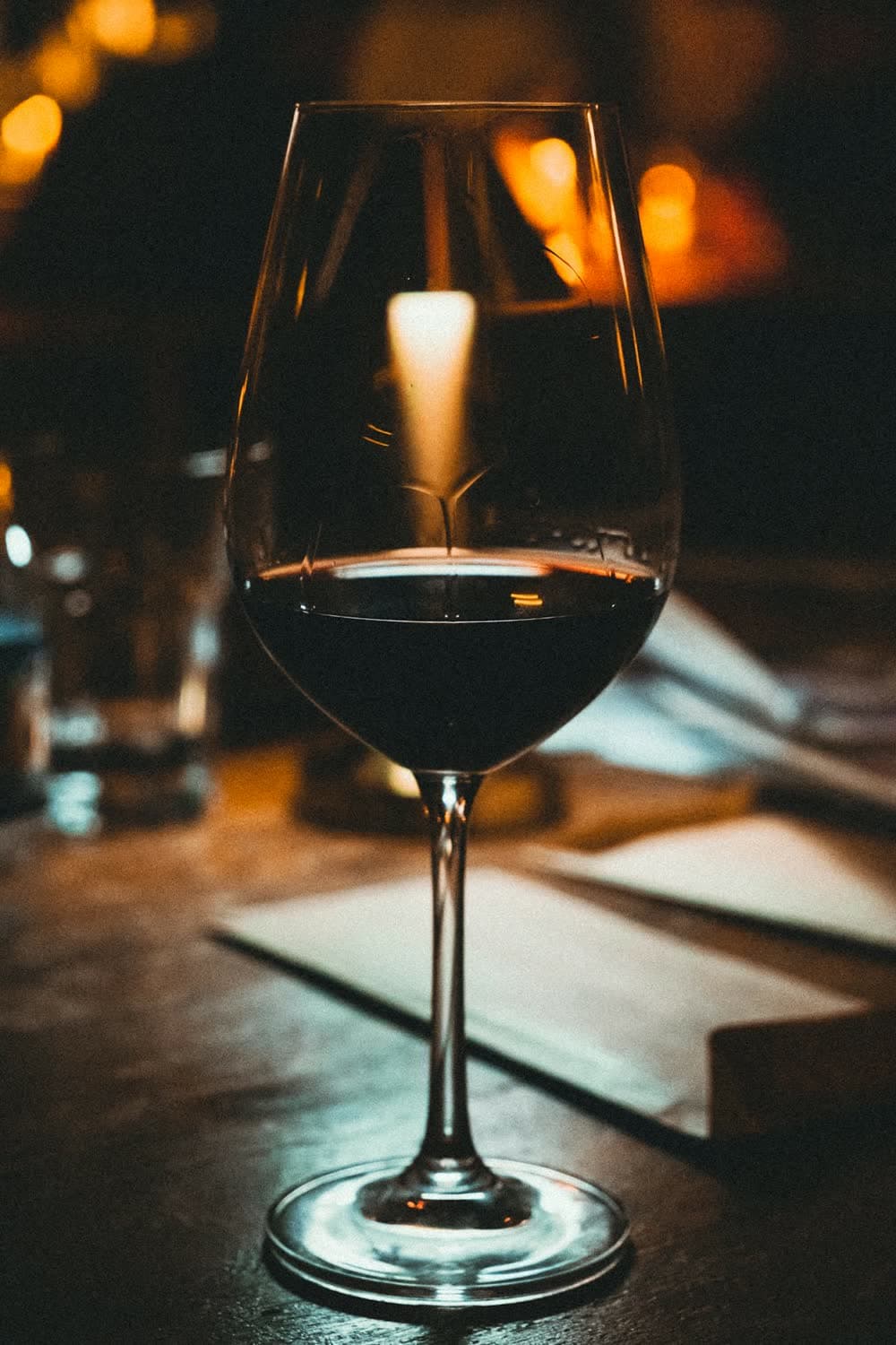 Un verre de vin rouge sur une table, une bougie allumée derrière