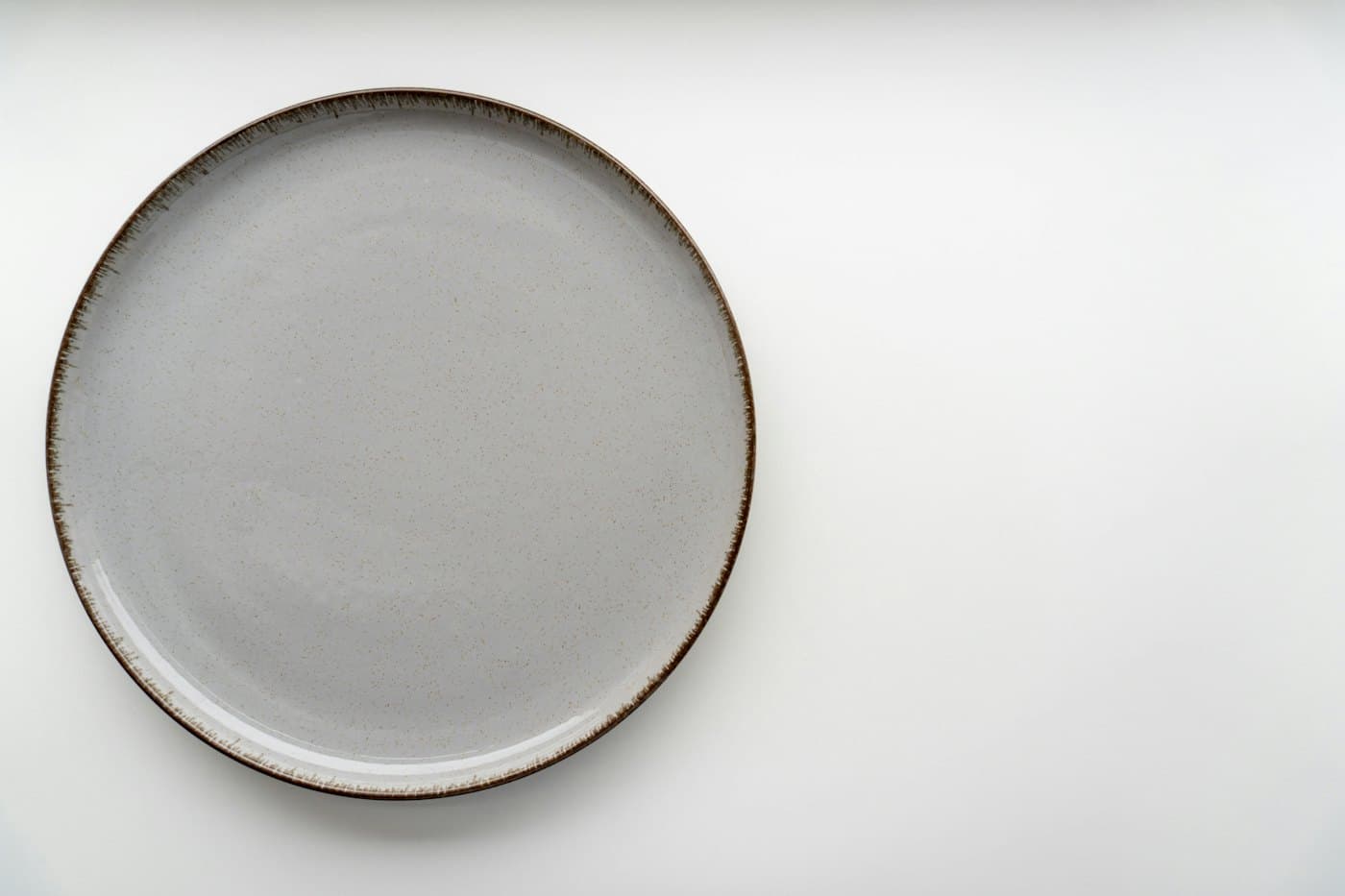 Assiette gris perle au liseré brun vue du dessus sur fond blanc