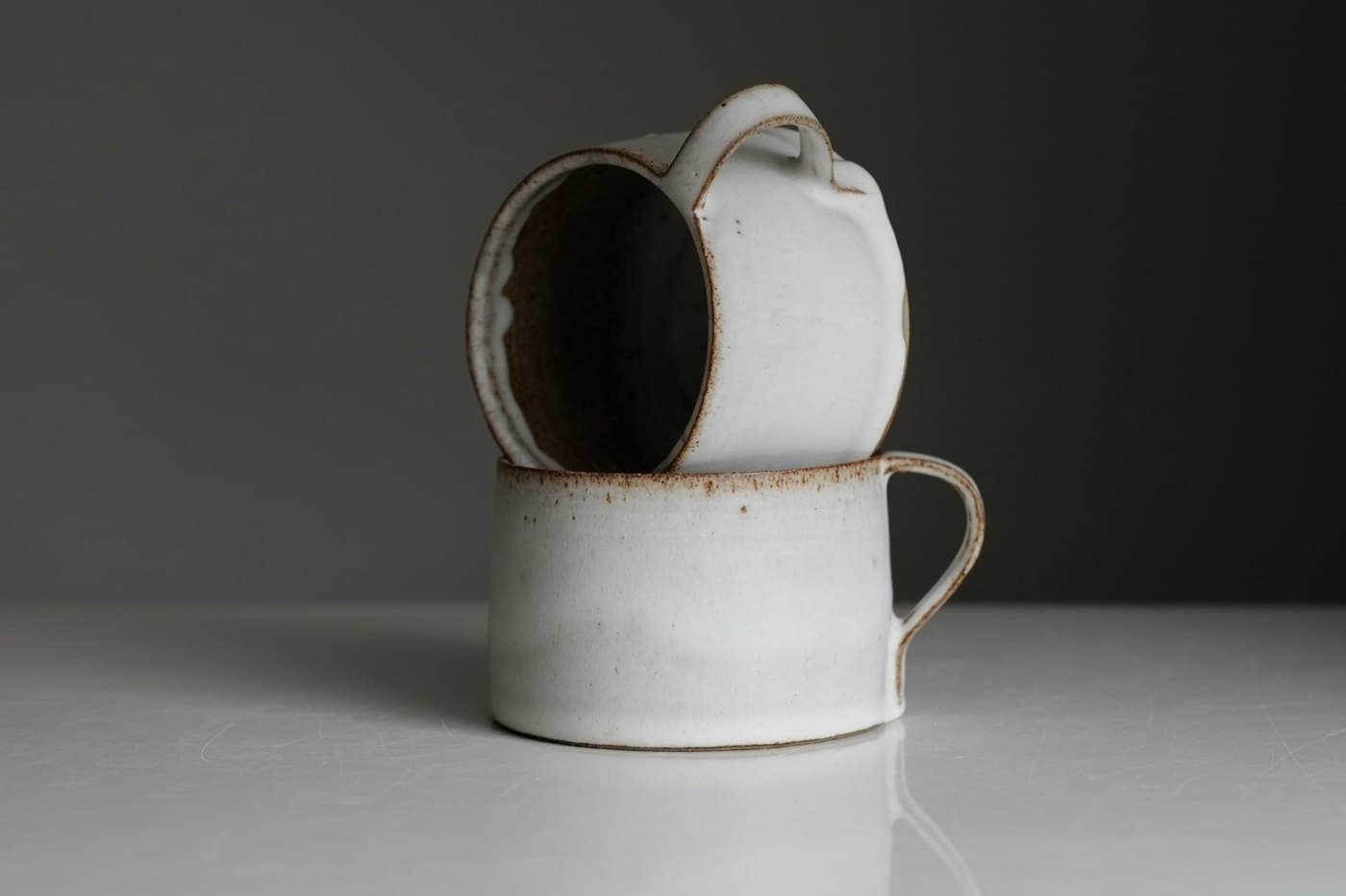 Deux tasses blanches à anse empilées l'une sur l'autre, sur fond gris sombre