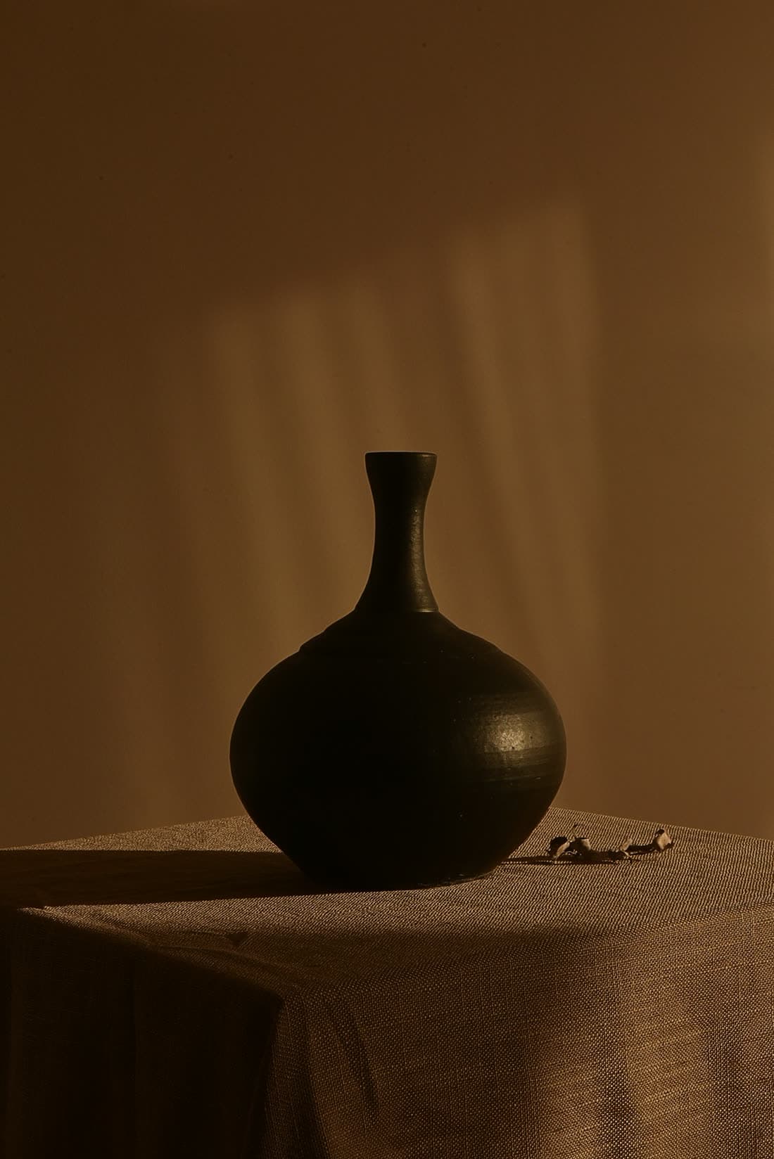 Vase noir à panse ronde et col fin posé sur une table couverte d'un drap brun