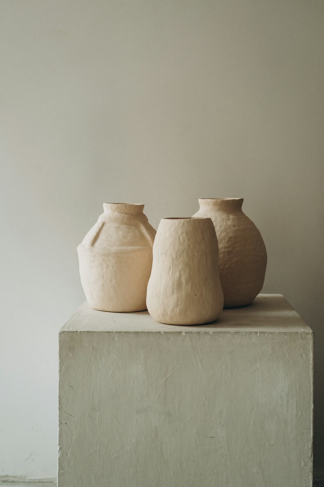 Trois petits vases en grès brut martelé posés sur un socle de béton clair
