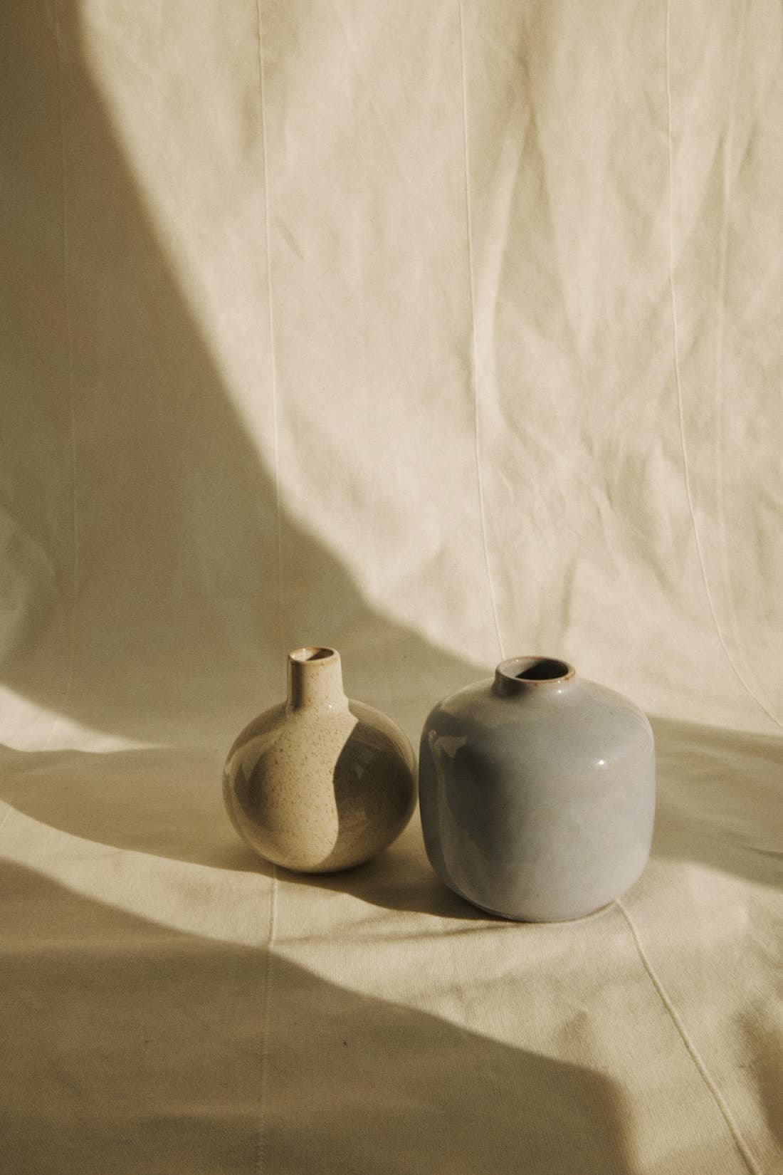 Deux petits vases, un crème et un gris, sur un drap de lin dans une lumière dorée