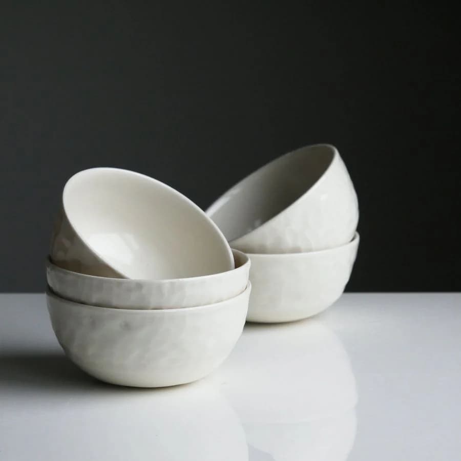Démonstration fictive : des bols blancs mouchetés, empilés sur une table blanche.