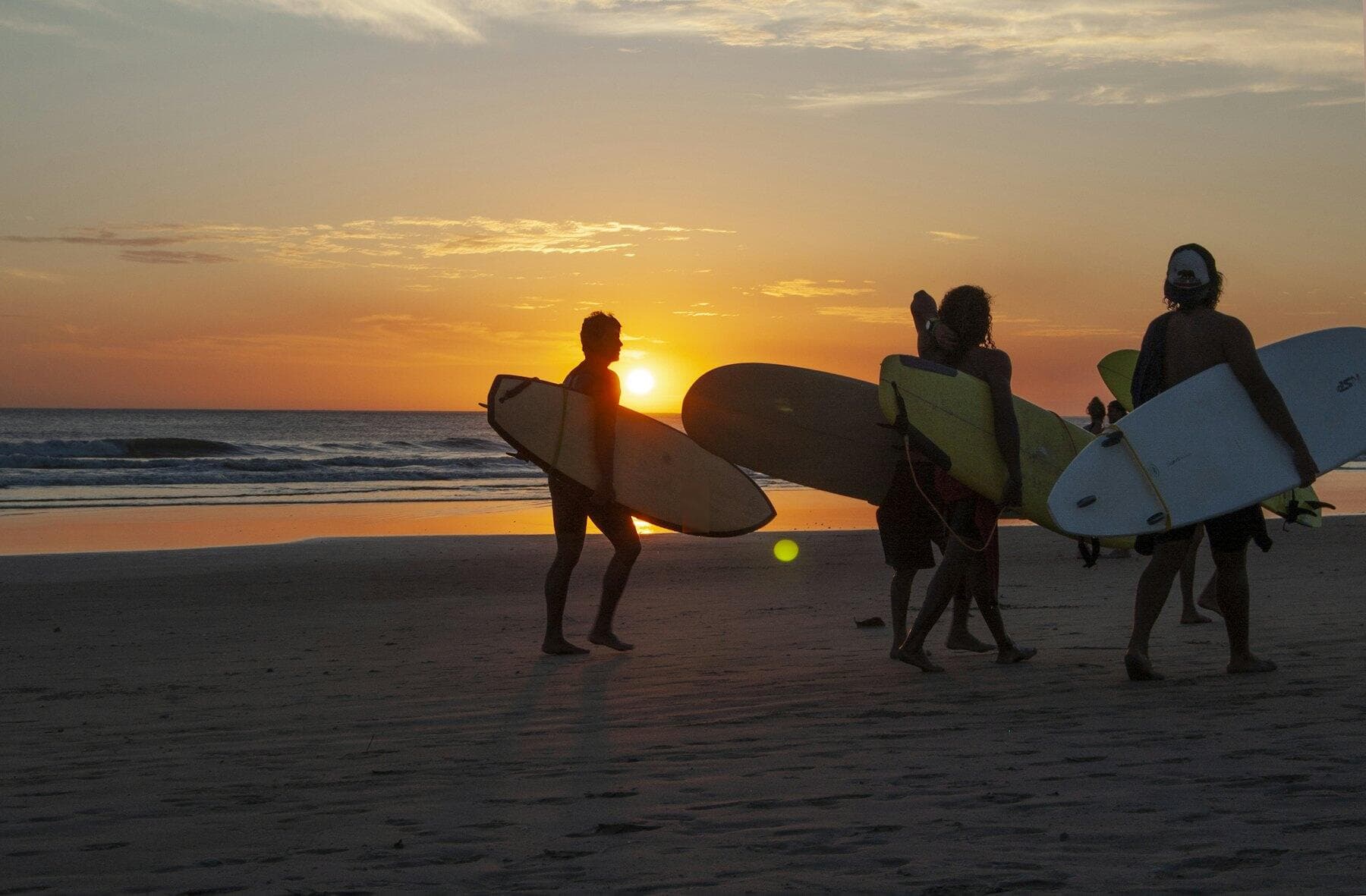 Les moniteurs, en silhouette, marchent sur la plage leurs planches sous le bras, au coucher du soleil