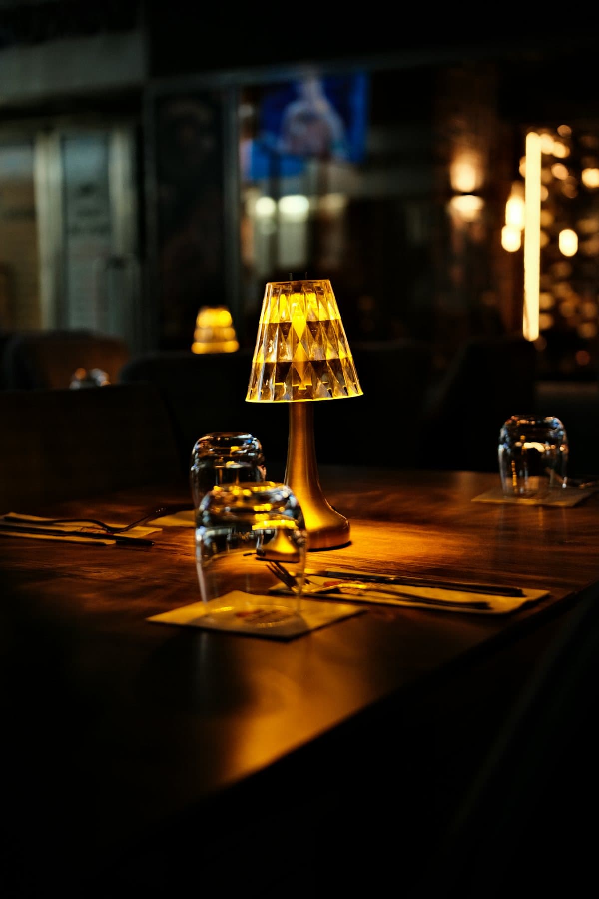 Une petite lampe dorée allumée sur une table dressée, dans une salle plongée dans la pénombre