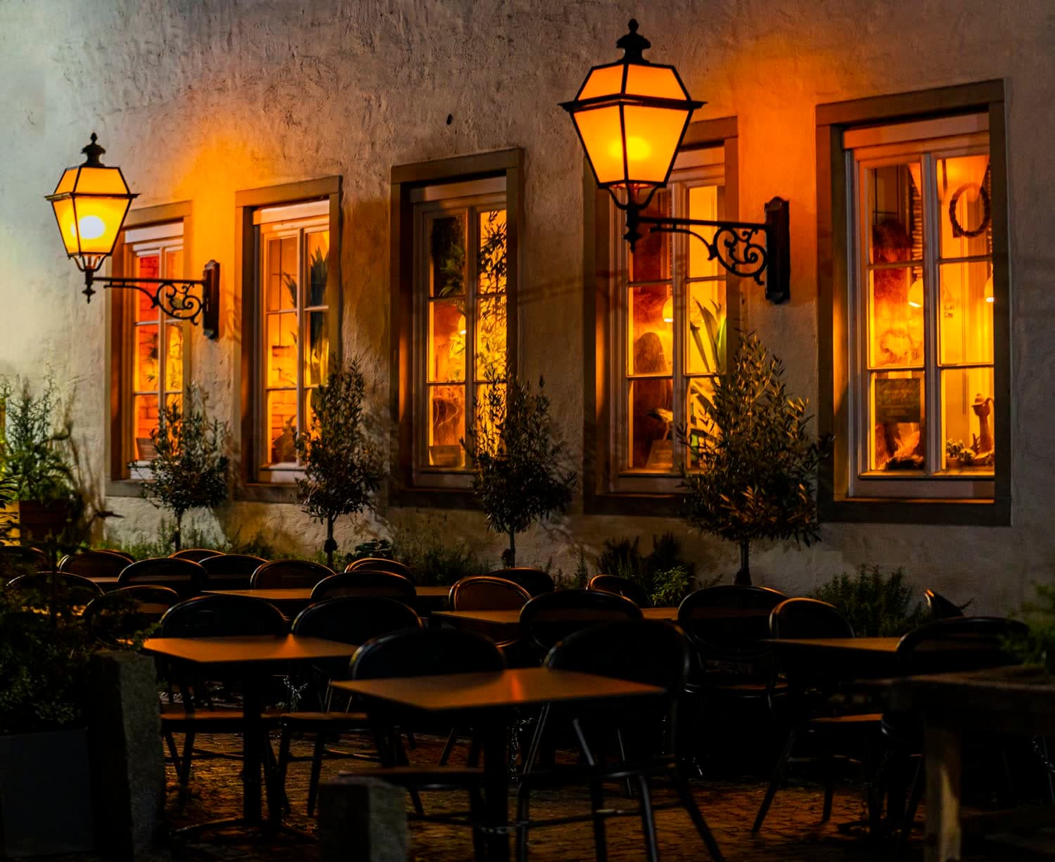 Une façade ancienne aux fenêtres éclairées et ses lanternes, la terrasse dressée à la nuit tombée